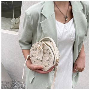 Detail of floral embroidery on cream woven straw round crossbody bag held by a model