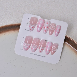 Detail of pink almond fake nails with strawberry patterns, pearls, and 3D bow accents