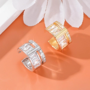 Elegant gold and silver ear cuffs with sparkling transparent crystals on an orange background