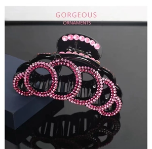 Close-up of black hair claw clip with sparkling pink rhinestones on a dark reflective surface