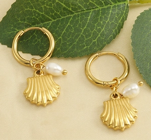 Détail de boucles d'oreilles coquillages dorées 18 carats avec perles sur fond texturé
