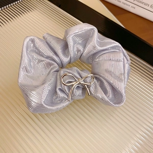 Détail d'un chouchou plissé violet avec nœud métallique argenté sur plateau en verre