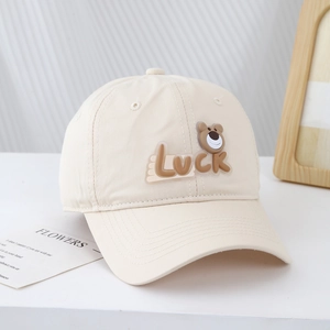 Close-up of beige cotton baseball cap with Luck lettering and cute bear patch