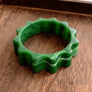 Détail macro du bracelet fleur en acrylique vert avec texture marbrée sur plateau bois