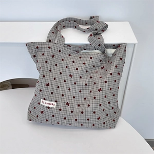 Detailed view of canvas tote bag featuring grey plaid, red polka dots, and bow embroidery