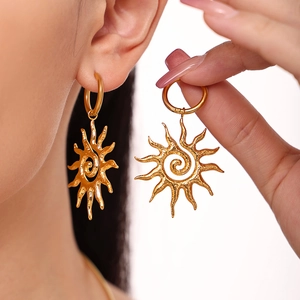 Golden sun-shaped spiral drop earrings with radiant rays worn by a model in a natural setting