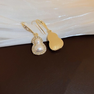 Detail of gold gourd earrings with white pearls and sparkling crystals on silk background