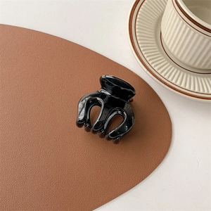Glossy black hair claw clip resting on a premium brown leather mat in a home setting
