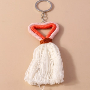 Detail showing handmade woven heart keychain with orange-pink cord and white cotton tassels