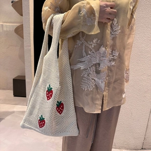 Detail of white crochet knit tote bag featuring red strawberry embroidery and mesh design