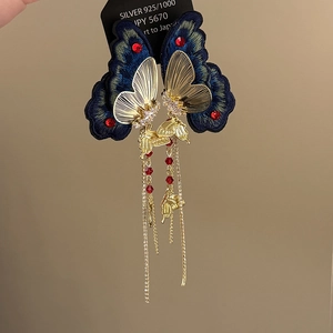 Detail of vintage blue butterfly embroidery earrings with gold tassel and red bead accents