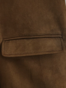 Détail macro de la veste en daim marron montrant le rabat de la poche et les coutures nettes