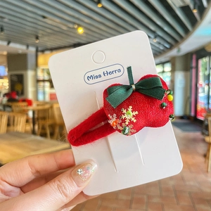 Détail d'une pince à cheveux pomme de Noël en peluche rouge avec nœud vert et paillettes
