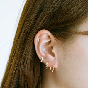 Close-up of a golden ear piercing set featuring crystal studs and textured hoops on an ear