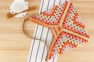 Detail of pink and orange crochet tote bag with leather strap on a wooden table