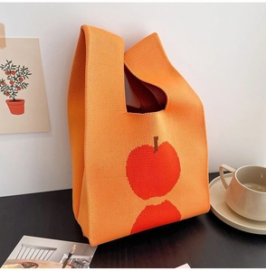 Detailed knit texture of orange tote bag with red apple pattern in a lifestyle setting