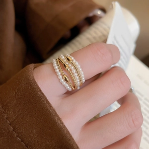 Close-up of multilayer ring featuring pearls and gold beads on a finger with elegant backdrop