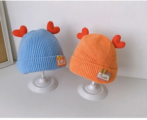 Close-up of knit baby hats in blue and orange with 3D red heart details on a stand