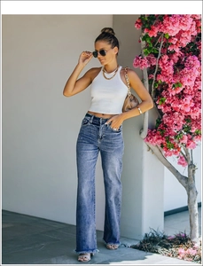 Detail of blue flare jeans with distressed rips and a white ribbed halter knit top