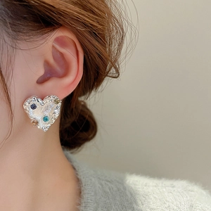 Detail shot of heart-shaped silver earrings with colorful rhinestones on a model
