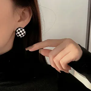 Minimalist black and white checkerboard round stud earrings worn by a model in a close-up view