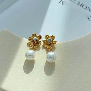 Orecchini a fiore dorato con pietra turchese e perle su un supporto in ceramica