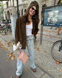 Close-up of brown suede jacket texture paired with a pearl chain belt and blue denim jeans