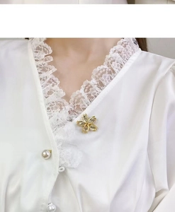 Close-up of a floral alloy brooch with pearls and rhinestones on a white lace shirt