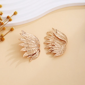 Detailed view of gold wing-shaped earrings with hammered metal texture on beige background
