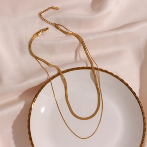 Detailed close-up of a double-layered 18K gold plated snake chain necklace on a ceramic plate