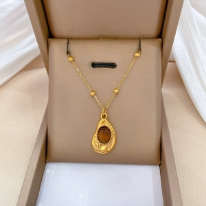 Close-up of a gold-plated irregular pendant necklace with a brown gemstone in a box