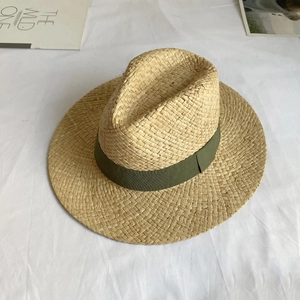 Top view of woven raffia sun hat featuring a dark green ribbon on white fabric