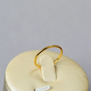 Detailed view of a slender gold-plated wave ring on a minimalist beige jewelry stand