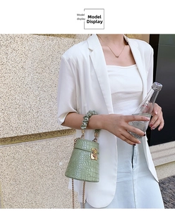 Detail of light green crocodile embossed bucket bag with gold lock and ruched handle