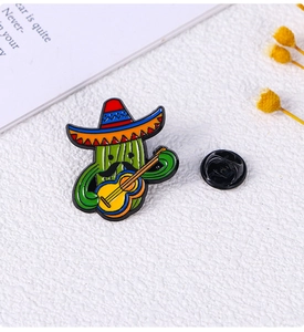 Detail of cartoon cactus enamel pin with guitar and sombrero on white textured background
