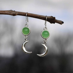 Detalle de pendientes de luna plateados con piedras verdes colgados de una rama
