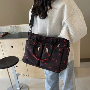Black nylon tote bag with red cherry print and multiple pockets shown on model's shoulder