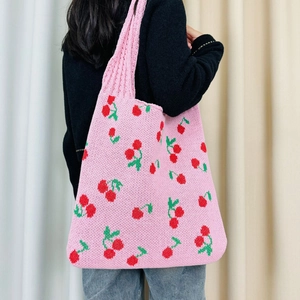 Close-up of pink knitted tote bag with red cherry patterns worn by a model