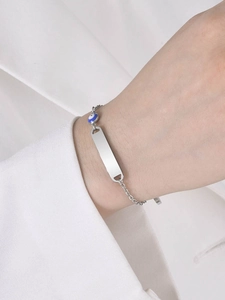 Detailed shot of a silver evil eye bracelet with a blank ID tag on a person's wrist