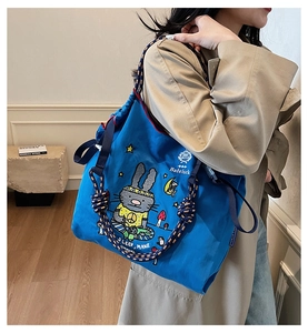 Detail of blue canvas tote bag featuring rabbit embroidery and colorful rope straps