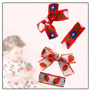 Detail of cute embroidered floral and strawberry hair clips on a toddler model