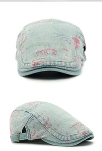 Close-up of denim flat cap with pink spray paint detail and side metal buckle