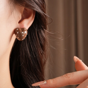 Close-up of heart-shaped brown earrings with white polka dots worn by a model