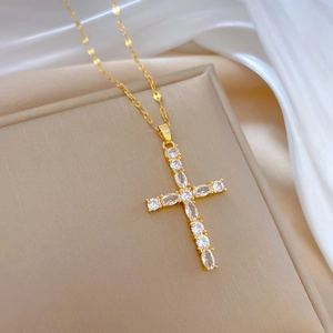 Close-up of gold-plated cross necklace with sparkling crystals on soft silk background