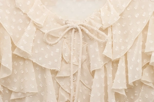 Detailed close-up of Swiss dot fabric, tiered ruffles and bow tie collar on beige blouse