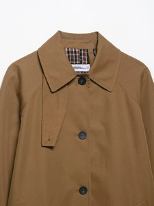 Close-up of lapel and button detail on a brown trench coat with stitched shoulder texture