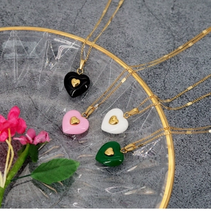 Detail of four colorful heart pendants in black, pink, white, and green on gold necklaces