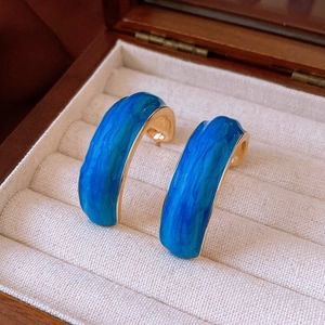 Detail of vintage blue enamel C-shaped flower earrings on soft beige velvet lining