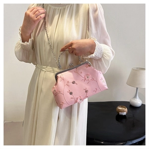 Detailed view of pink embroidered silk evening clutch bag held by an elegant female model