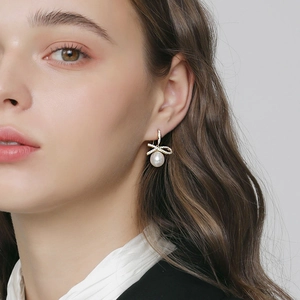 Elegant gold bow earrings with crystal pavé and white pearls worn by model
